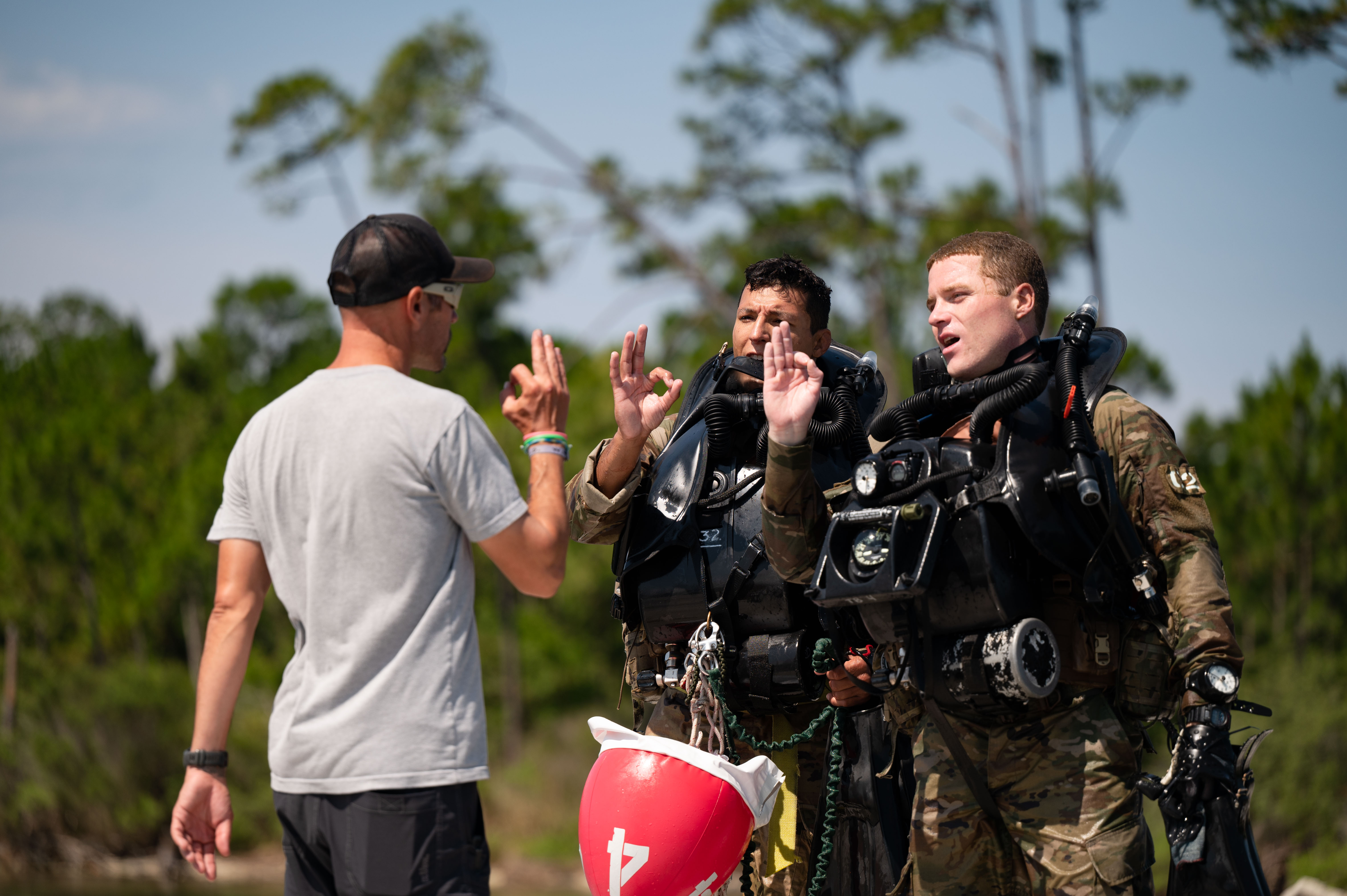 Instructor giving hand signals to two dive school students in dive gear